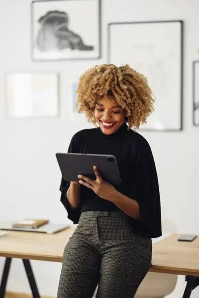 Cheerful African American woman, sitting on her desk, smiling and using her laptop. She is typing something.